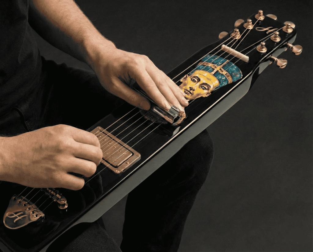 Guitarra havaiana sendo tocada com slide e arte de Nefertiti no instrumento
